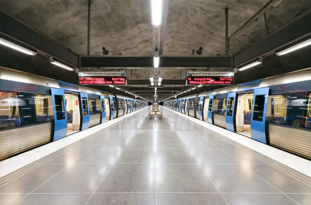 Modern underground train station with trains on both sides of a central platform, viewed from the middle of the station.